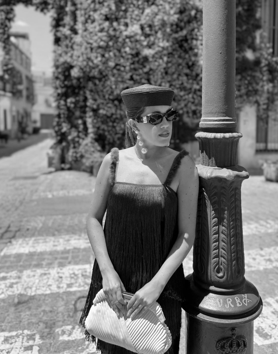 Mujer invitada de evento especial vestida con un top y falda de flecos con tocado y pendientes de perlas, bolso de mano a juego con el look y gafas de sol
